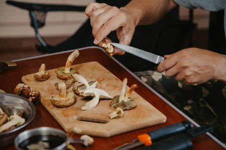 Processing of collected mushrooms. Male hands cut fresh edible white mushrooms on a wooden boardの写真素材