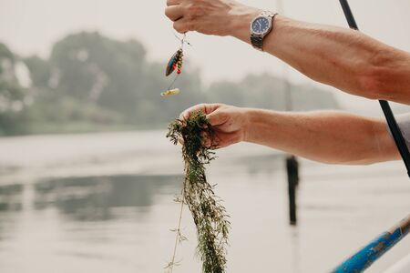 Unsuccessful catch. Hand shoots green river algae that are hooked onto the hook of a fisherman's fishing pole above the water surface.の写真素材