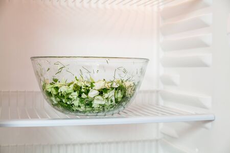 Healthy food. On the shelf of an empty refrigerator stands a glass bowl with chopped vegetables close upの写真素材