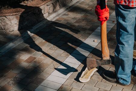 Dangerous shadow. A man in a red checkered shirt holds an ax in his hand in the yard. A deceptive...