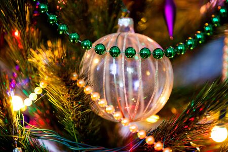 Exquisite transparent striped ball decoration toy hanging on Christmas tree. Pine decorated with a garland of light bulbsの写真素材