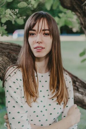 Portrait of a long-haired girl. A pretty girl in a white dress leans on a tree branch on a summer...