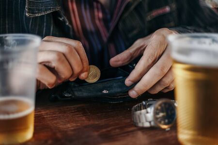 Coins for beer. Hands take out a yellow coin from the wallet. On the sides on the table are two plastic glasses of beer.の写真素材