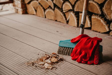 Autumn still life. A brush stands on the floor of a clean veranda. On top are red work gloves. Before her a bunch of garbage collected.の写真素材