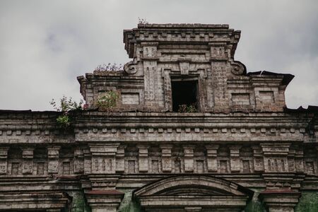dilapidated superstructure on the roof of an abandoned non-residential building against a cloudy sky closeup. Sprouted green plants are visible on the roofの写真素材