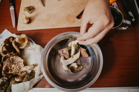 left hand puts chopped edible mushrooms in a metal bowlの写真素材