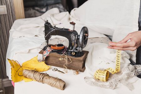 Workplace seamstress. Vintage sewing machine and a skein of threads. A yellow maple leaf lies next to it. The woman's hands fold a flexible tapeの写真素材