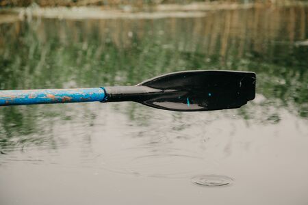 Black plastic paddle paddles over the water after a close-up stroke. Water drops flow down