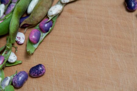 Pods and bean seeds of different colors lie on the edge of a wooden board. View from aboveの写真素材