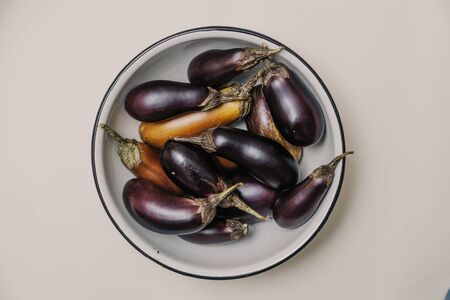 group of blue and brown ripe eggplants with green ponytails lie in a round metal plate on a white background. Close-up. View from aboveの写真素材
