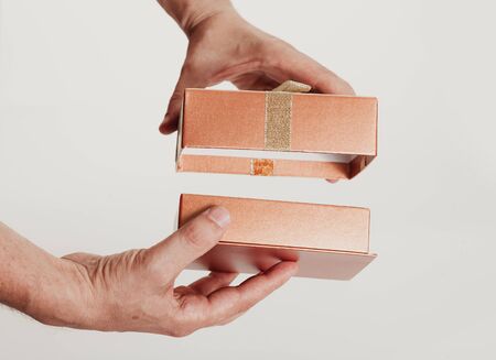 Hands understand the cover of a beautiful box for a gift with a bow from a gold ribbon on a white...