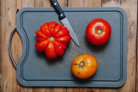 Vegetable still life. Ribbed red and yellow tomatoes lie on a gray cutting board. Nearby lies a sharp knife. View from above
の写真素材