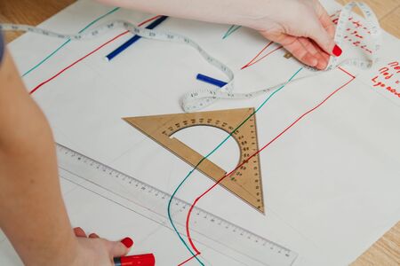 Designer creates a model. Female hands with a manicure draw a sewing pattern on paper