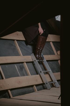 slender girl in high leather boots stands on planed wooden boards. The left hand rests on the kneeの写真素材