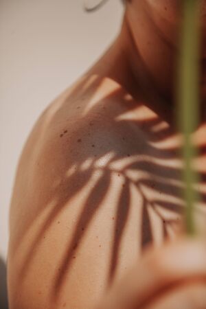 Shadow on the shoulder. A shadow from a branch of a palm tree with thin leaves falls on her shined tanned shoulders.の写真素材
