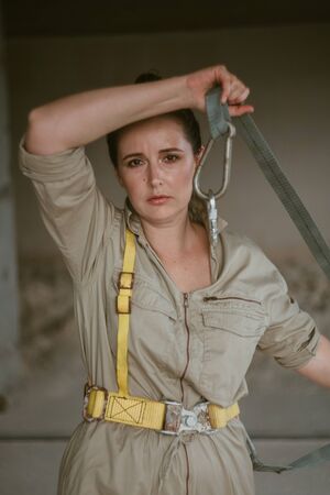 nice girl in gray overalls holds a safety belt with a carbine in her hands. Portrait of a woman...