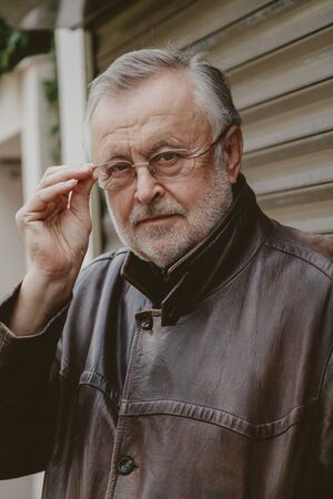 Portrait of a man with a gray beard. Elderly man in glasses and a leather jacket in autumn afternoon