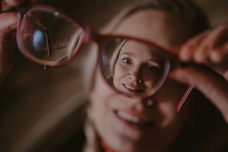 original angle. Stylish blonde holds optical glasses. Through the glass you can see a pretty face....