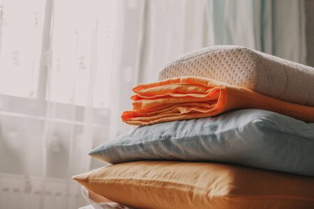 Linens and pillows of different colors and sizes are stacked in front of the bedroom windowの写真素材