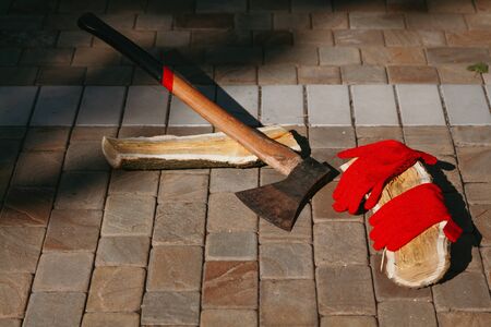 ax on a long handle and chopped mulberry log lie in the courtyard on paving slabs. Red gloves are on...