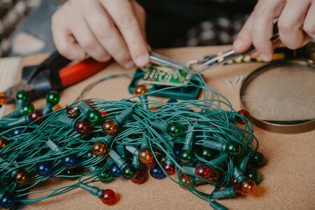 folded garland with electric round bulbs lies on a table close-up. Back blurred image of hands with...