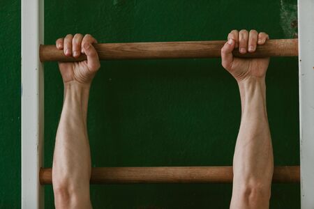 Gymnast's hands hold tightly on the horizontal bar of the Swedish wall in the gym close-up