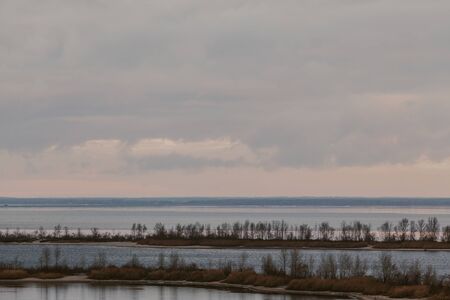 Beautiful landscape of a wide river on a winter day. In parallel narrow sections of land, trees...