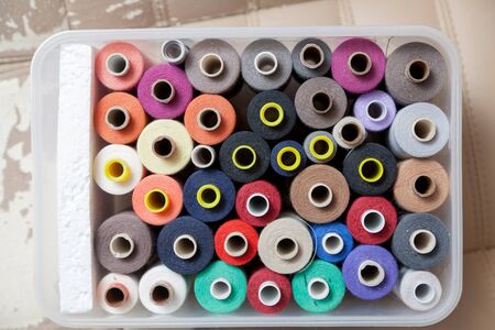 Spools of thread of different colors and diameters stand tightly together in a plastic box. View from above
の写真素材