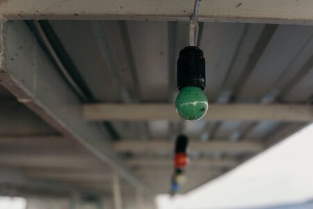 Green colored incandescent bulb weighs under the ceiling of a metal profile closeup