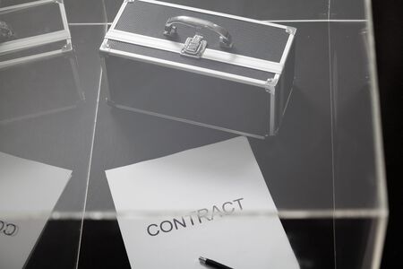 Transparent business. A contract printed on paper and a portable safe for money lies in a glass box. The pen is on top of the contractの写真素材