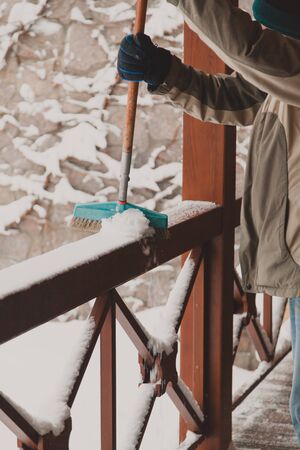 Cleaning on the winter terrace. The owner brushes the wooden snow veranda from the snow with a wooden handle
の写真素材