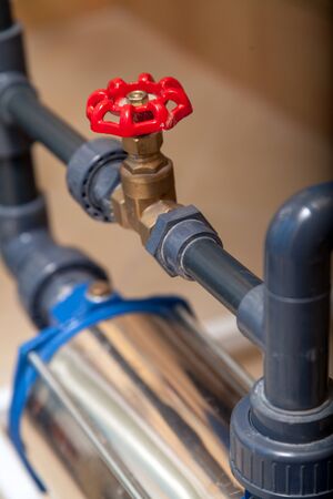 Close-up beautiful vertical brass valve water tap with a red round handle on a plastic pipeの写真素材