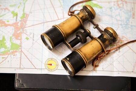 Still life with binoculars and a map. Vintage metal binoculars lie on topographic map of the area. A...