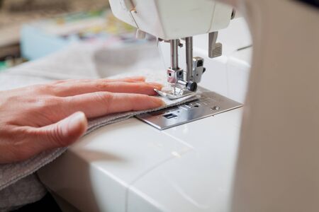 Seamstress at work. Seamstress's left hand makes a seam on a soft fabric using a sewing machine...