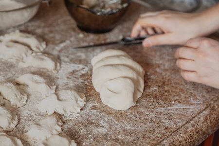 piece of dough lies on the granite countertop. Nearby lie raw dumplings in white flour