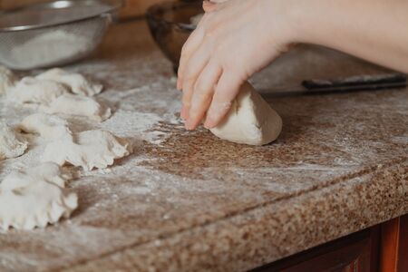 woman's hands crumple a piece on the granite countertop. Nearby lie dumplings in white flourの写真素材