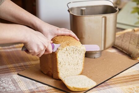 woman hands are cut with a large lilac knife with the teeth of a loaf of bread close-up