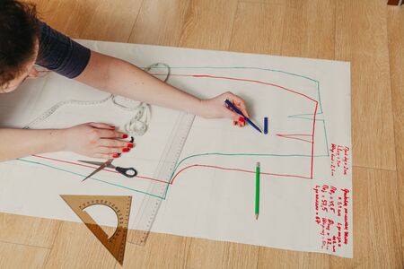 Designer creates a model. Female hands with a manicure do the layout of the sewing pattern on paper