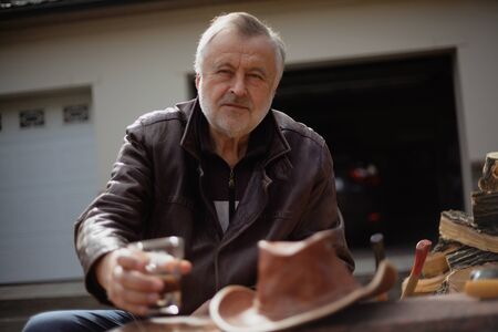 Portrait of a man with a gray beard. Close-up of an elderly man in a leather jacket on an autumn day. Rear open garageの写真素材