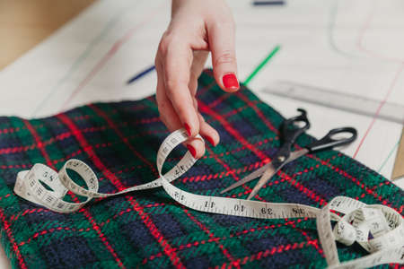 Designer creates a model. Female hands with a manicure make markings on a piece of Scottish fabric.