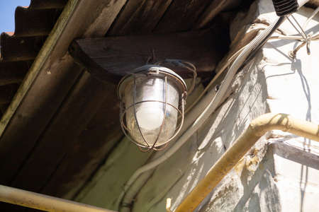 lamp with a semicircular shade weighs under the roof on a white wall. Nearby electrical wires and a gas pipeの写真素材
