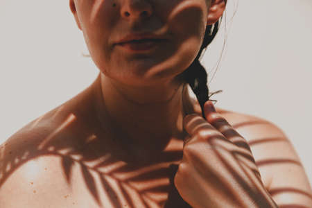 shadow from a branch of a palm tree with thin leaves falls on the drenched tanned shoulders and face...