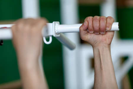 Gymnast's hand hold tightly on a horizontal bar of a metal exercise machine in a sports hall...