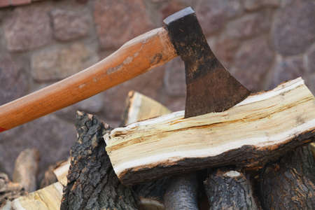 ax on a long handle sticks out in a mulberry wood log. A log lies on a pile of chopped firewood in the yardの写真素材