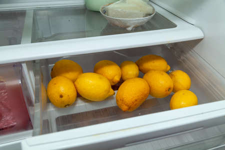 Vitamins for disease prevention. Several yellow lemons lie in a transparent plastic container of the refrigeratorの写真素材