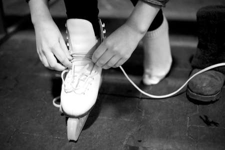 Hands tie a long lace on a white leather shoe of a modern skate. Monochrome image