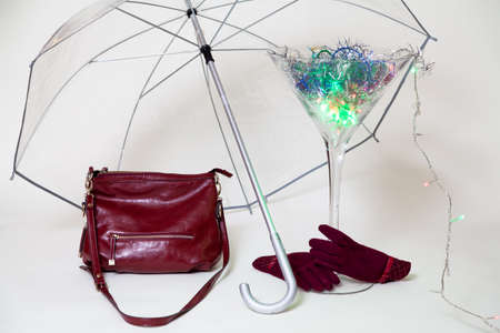 Invisible hands in red gloves hold a large martini glass from below. A magic cocktail glows inside the glass. There is a transparent umbrella over the glass. Nearby is a red women bagの写真素材