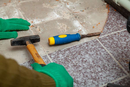 dismantling of tile. Hands in green working gloves undermine the tile with a chisel and a hammerの写真素材