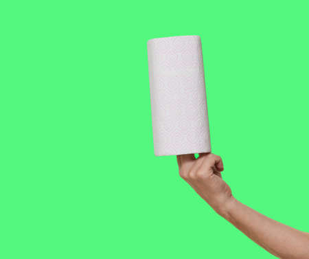 roll of white paper towels is held vertically on the fingers of the right hand isolated on green...