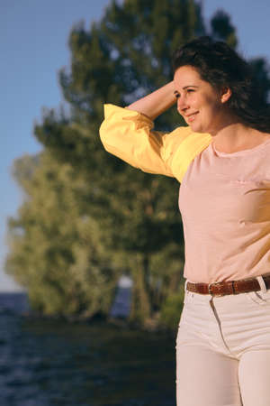 Portrait of a pretty girl with long red hair and a bright yellow jacket on the sandy beach of a wide...
